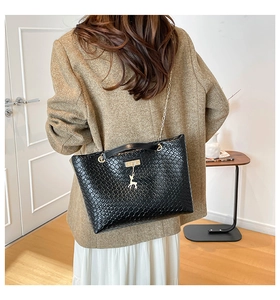 Detail of black textured shoulder bag with golden deer pendant and metal chain strap