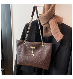 Detail of dark brown woven tote bag with gold deer pendant and chain strap on black blazer