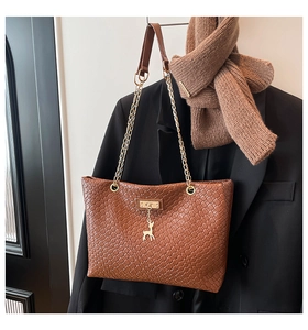 Detail of brown woven tote bag featuring gold chain strap and cute deer charm pendant