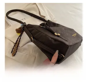 Detail of dark brown tote bag with bear charm and striped ribbon on white suit