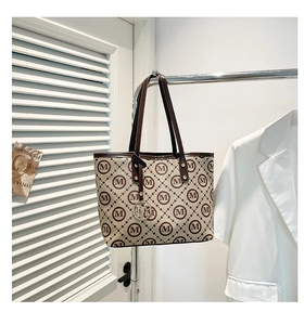 Détail du cabas en toile avec motif M et anses en cuir sur un cintre de mode