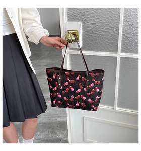 Detalle del bolso tote con estampado de cerezas y asas de cuero en una puerta blanca