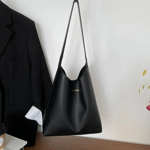 Bolso tote negro mate con letras doradas colgado junto a una chaqueta de traje