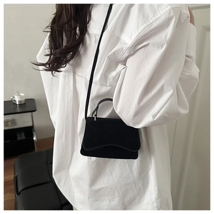 Minimalist black suede crossbody bag with curved flap shown on model in a modern room