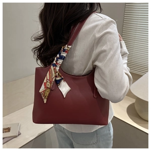 Detail of burgundy leather tote bag featuring contrast stitching and floral silk scarf accessory