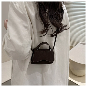 Détail du micro sac bandoulière marron foncé en daim porté sur une chemise blanche oversize