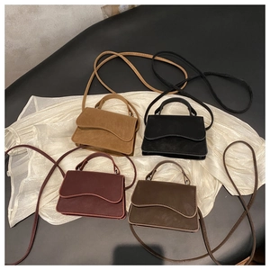 Flat lay of multiple wave-flap crossbody bags in various colors on white silk fabric