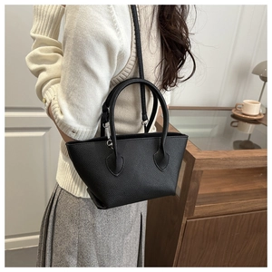 Close-up of black litchi pattern leather bucket bag worn on shoulder by a model