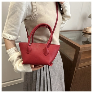 Red lychee textured bucket bag with double handles and adjustable shoulder strap worn by model