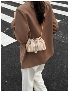 Detail of knitted bucket bag with pearl drawstring and golden chain strap in street view