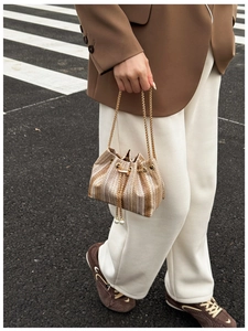 Detail of woven bucket bag with elegant gold chain strap and decorative pearl tassels