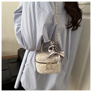 Detail of mini quilted beige chain bag with silk scarf handle on striped shirt