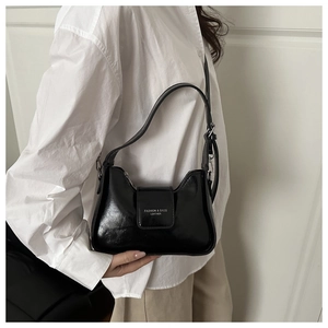 Détail du sac sous le bras noir brillant montrant le cuir poli et le rabat avec logo blanc