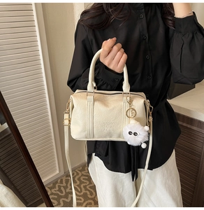 Détail du sac Boston en cuir beige avec texte embossé et pendentif en peluche