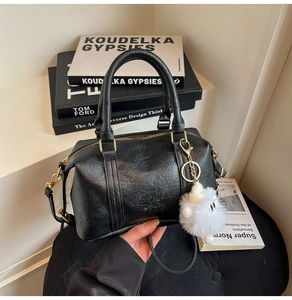 Détail du sac Boston en cuir noir avec ferrures dorées et breloque en fourrure blanche