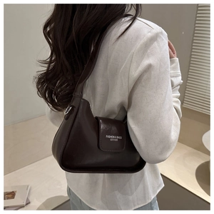 Close-up of a minimalist dark brown leather crescent bag worn on a shoulder