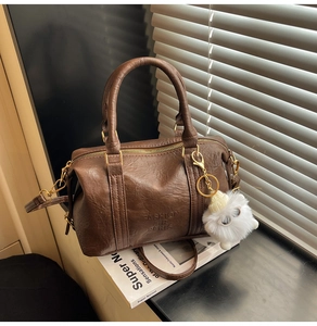 Détail d'un sac en cuir marron avec charme en peluche et bandoulière réglable