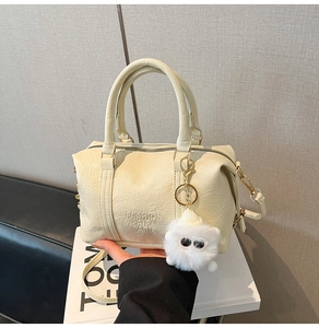 Detail of cream white leather bag with vintage texture and plush charm on white books