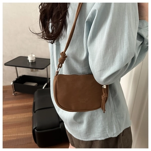 Brown leather half-moon crossbody bag with embossed logo and knotted shoulder strap detail