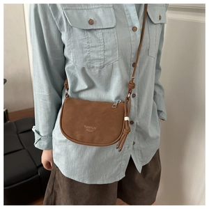 Detailed close-up of brown matte saddle bag with logo and knot design on blue shirt