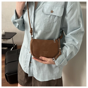 Detailed view of brown leather crossbody bag featuring embossed logo and silver zipper