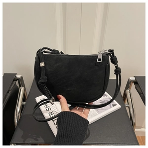 Detail of a black matte crescent bag featuring a knotted strap and chic metal letter charm