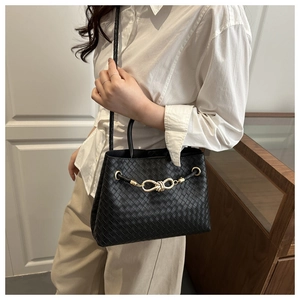 Detail of woven black leather tote with gold knot buckle shown on model in soft light