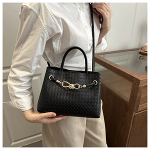 Detailed view of black woven leather handbag with golden knot buckle and dual straps