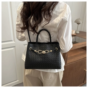 Detailed view of black woven leather handbag with gold knot hardware and crossbody strap