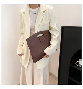 Detail view of dark brown pebbled leather briefcase held by a model in a white textured blazer
