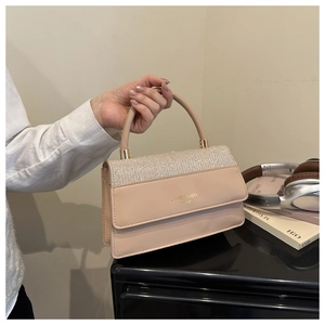Detail of beige handheld bag featuring a glitter flap and gold metal handle fixtures
