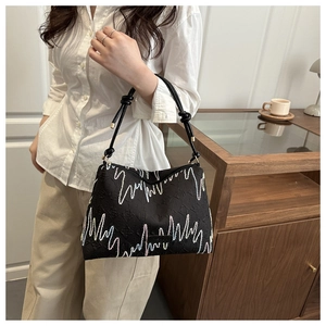 Detail of black tote bag featuring wave embroidery and knotted rope shoulder strap