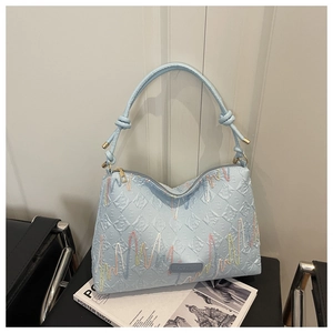 Detail of light blue embroidered tote bag with quilted pattern and fashion label