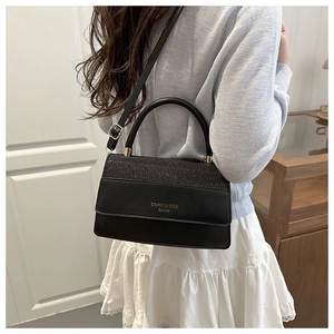 Detail of black crossbody bag with shimmering matte flap and gold hardware