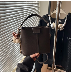 Nahaufnahme einer braunen Eimer-Tasche mit Bärenanhänger und stilvollem Lichtspiel