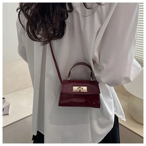Detail shot of the glossy burgundy leather crossbody bag with a gold metal lock system
