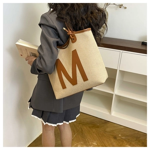 Detailed texture of beige woven tote bag with brown leather M patch on a model