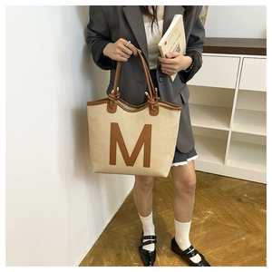 Detail of woven tote bag with brown leather M patch and minimalist knotted rope handle
