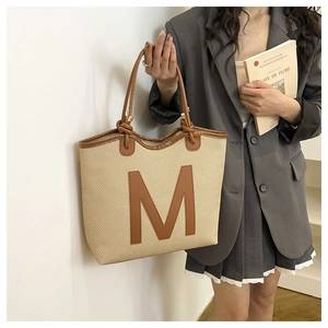 Detail of canvas tote bag featuring large leather M patch and brown knotted top handles