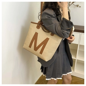 Detail of woven tote bag with brown leather M patch and knot strap detail for women