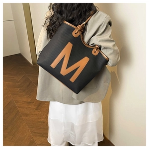 Detail of a large woven tote bag with a brown leather letter M and matching shoulder straps