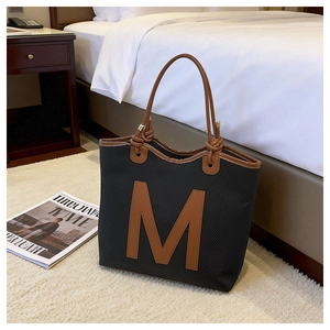 Detail of black woven tote bag with brown leather M patch and stylish knotted rope handle