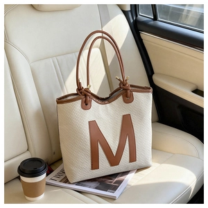 Detail of woven tote bag with brown leather M patch on a luxury car seat