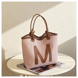 Detail of woven tote bag featuring a leather M patch and knot-style rope shoulder straps