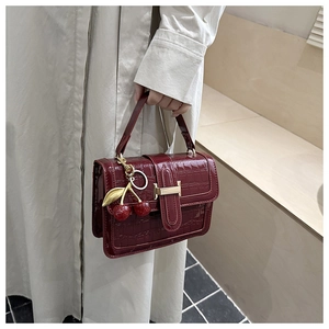 Close-up of deep burgundy crocodile embossed handbag with glossy finish and cherry charm