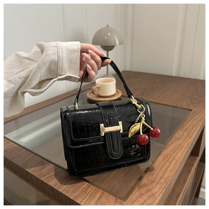 Close-up of black croc-embossed leather handbag with a red cherry charm and gold buckle