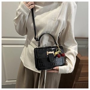Detail view of black crocodile pattern handbag with gold trim and red cherry pendant