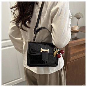Close-up of black crocodile embossed patent leather handbag with a red cherry pendant
