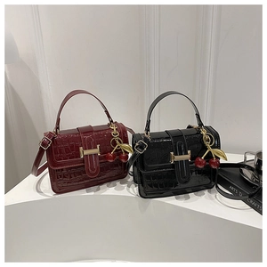 Detail view of glossy croc-embossed small crossbody bags with cherry charms in black and wine red
