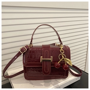 Close-up of burgundy glossy crocodile texture handbag with cherry charm and gold buckle